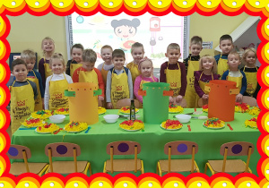 Na zdjęciu grupa dzieci w żółtych fartuchach kucharzy. Na stołach talerze ze spagetti.